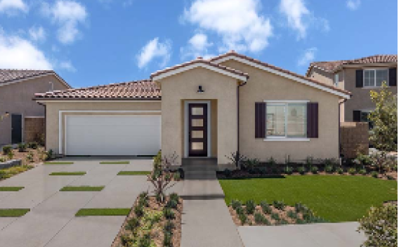 A modern single-story house with beige walls, a white garage door, and a dark front door. Neat lawn and paved driveway under a blue sky with scattered clouds.