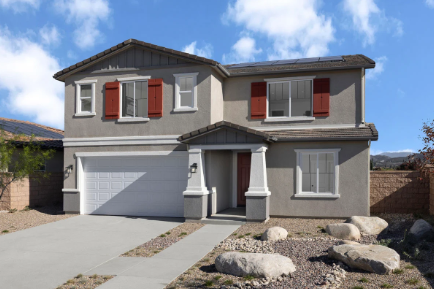 Two-story modern house with gray exterior, red shutters, white garage door, and a gravel yard with large rocks under a blue sky.